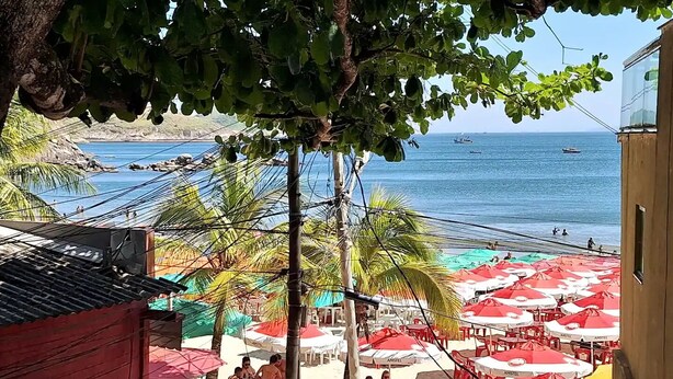Een restaurant aan het strand met terras en parasols, met uitzicht op zee.