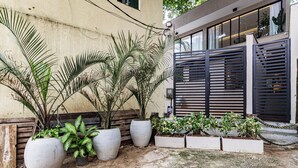 Een binnenplaats met grote potplanten, een houten bank en een modern gebouw met een metalen poort.