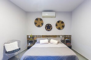 Habitación de hotel con cama, una silla, aire acondicionado instalado en la pared y platos decorativos.