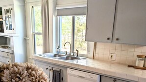 A kitchen with white cabinets, a sink, and a dishwasher. There is a vase with flowers on the counter. - Cozy Blue Cottage

 (Willcox)