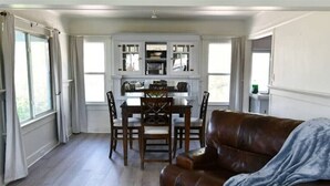 A spacious living room with a brown leather sofa and a dining area with a wooden table and chairs. - Cozy Blue Cottage

 (Willcox)