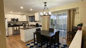 Uma cozinha espaçosa com eletrodomésticos modernos, uma área de refeições com mesa e cadeiras, e vista para uma varanda através de uma porta de correr.
