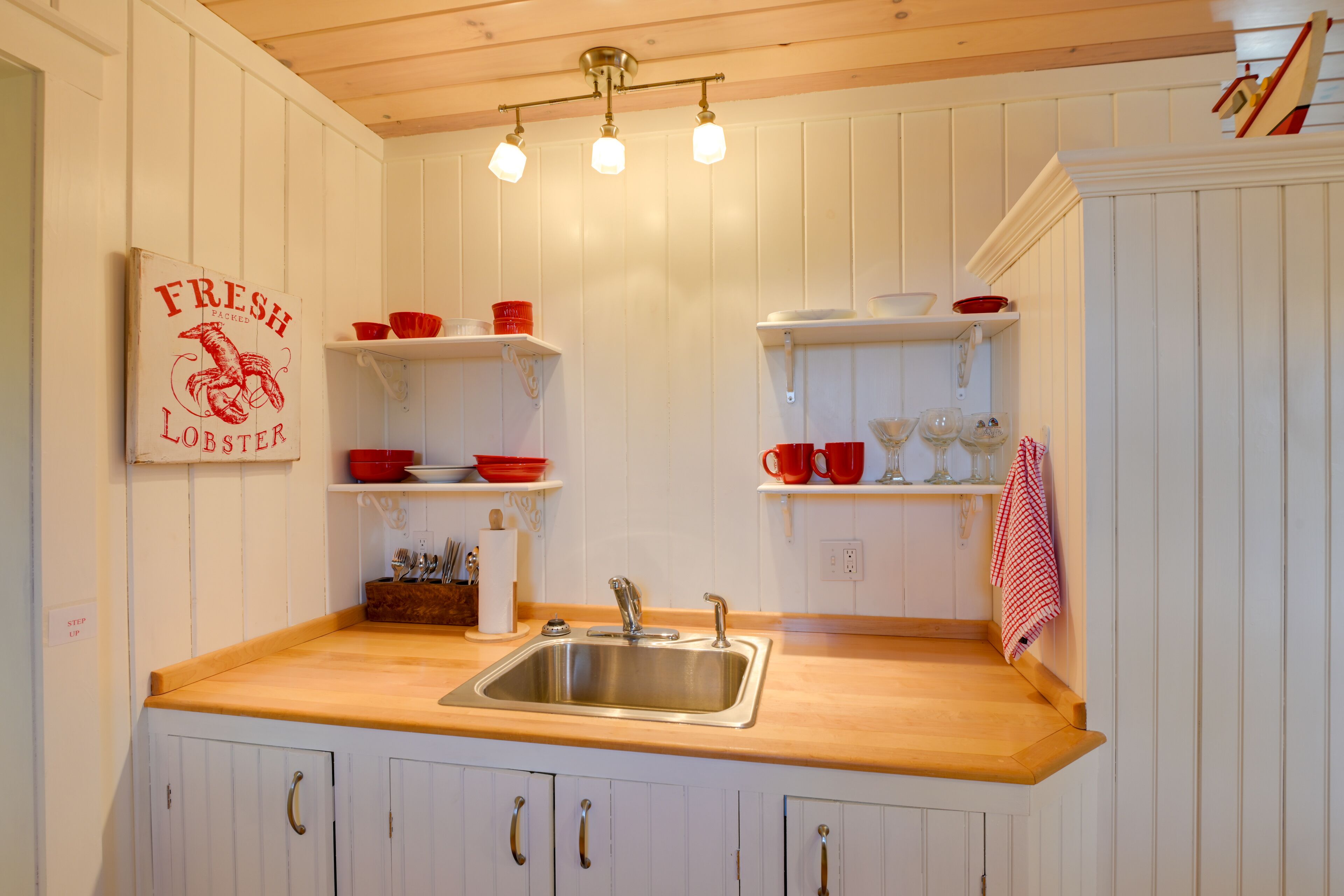 A kitchen with white cabinets, a wooden countertop, a stainless steel sink, and red and white kitchenware.