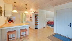 Una cocina moderna con armarios de madera, una isla central con taburetes, iluminación colgante y vistas a un comedor.