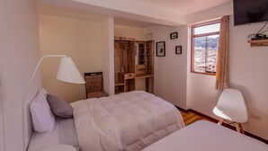 Un dormitorio con dos camas, un armario de madera, un televisor montado en la pared y una ventana con vistas a edificios.