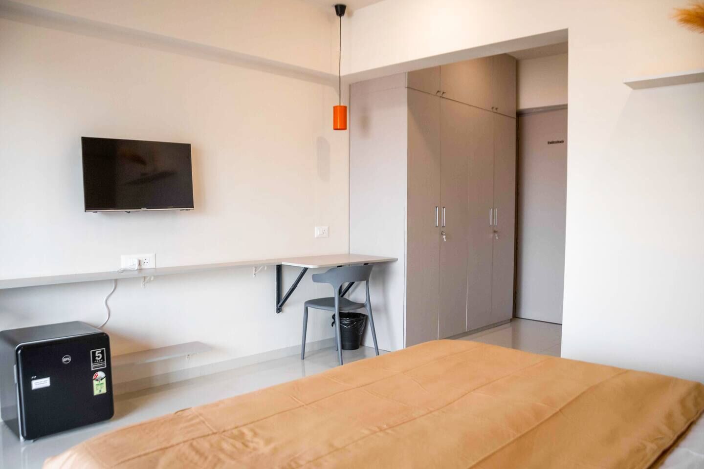 A modern bedroom with a bed, a desk, a chair, a TV, and a wardrobe.