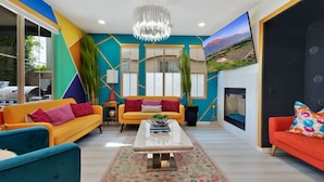 Un salon moderne agrémenté d’œuvres d’art géométriques aux couleurs vives, d’un grand téléviseur à écran plat, d’un lustre et d’une cheminée.