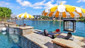 Un espace aménagé au bord de la piscine, avec des marches en pierre carrelée menant à l’eau, des sièges extérieurs et des parasols à rayures jaunes et blanches offrant de l’ombre.