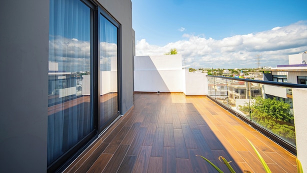 A modern balcony with wooden flooring, large windows, and a view of the cityscape. - Modern apartment in the center near the beaches (Playa del Carmen)
