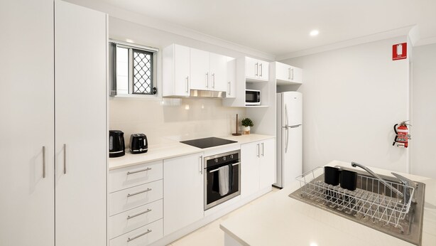 Una cucina moderna con mobili bianchi, un forno a microonde, un frigorifero, un lavello con scolapiatti e una finestra con inferriata decorativa.