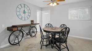 Een eethoek met een ronde houten tafel, vier stoelen, een fiets en een wandklok.