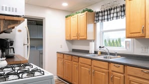A kitchen with wooden cabinets, a gas stove, a sink, and a window with a view of trees.