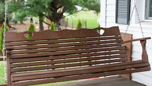 A wooden bench with heart-shaped cutouts on the backrest, suspended by chains.