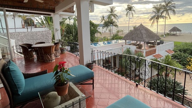 Un espacio de estar al aire libre cubierto con vistas a la playa y palmeras.