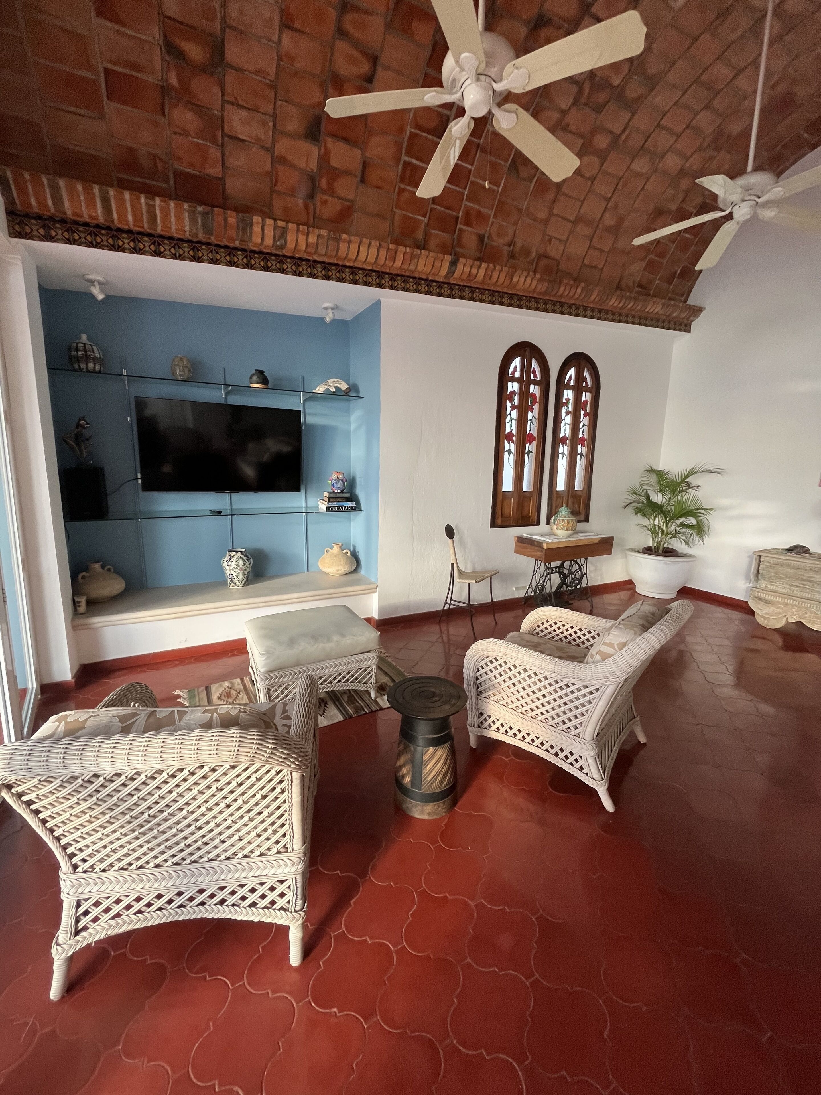 A living room with a television, wicker furniture, a ceiling fan, and a brick wall.