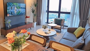 A modern living room with a flat-screen TV, a sofa, a coffee table, and a dining area with a vase of flowers.