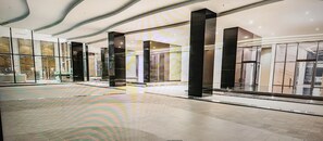 Un vestíbulo amplio con piso estampado, grandes ventanales de vidrio y pilares negros modernos.