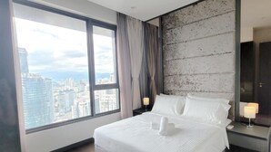 A modern hotel room with a large window offering a city view, a neatly made bed, and a nightstand with a lamp.