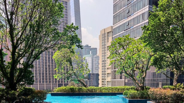 A swimming pool surrounded by greenery and modern buildings.