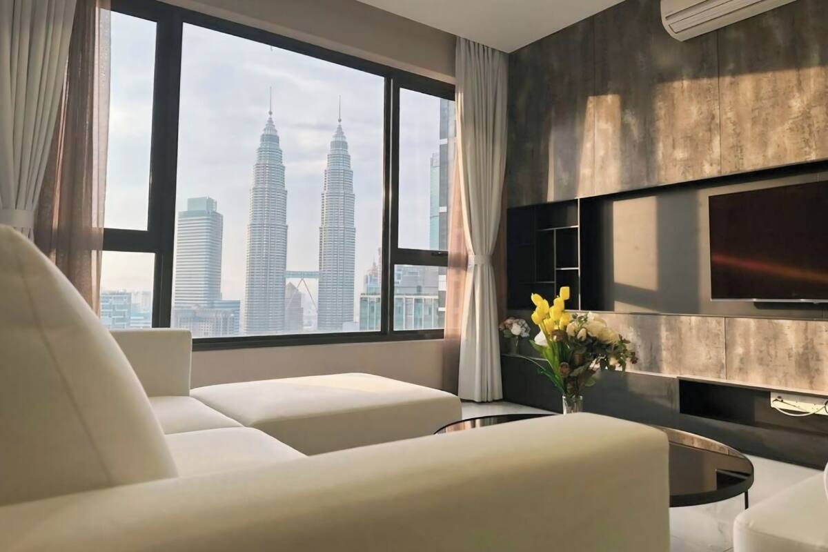 A modern living room with a large window, a flat-screen TV mounted on the wall, and a sofa.