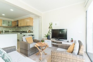 Ein modernes Wohnzimmer mit Rattanmöbeln, einem Flachbildfernseher und einer Küche im Hintergrund.