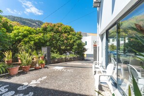 Un patio empedrado con plantas en macetas, la entrada de un edificio y montañas al fondo.