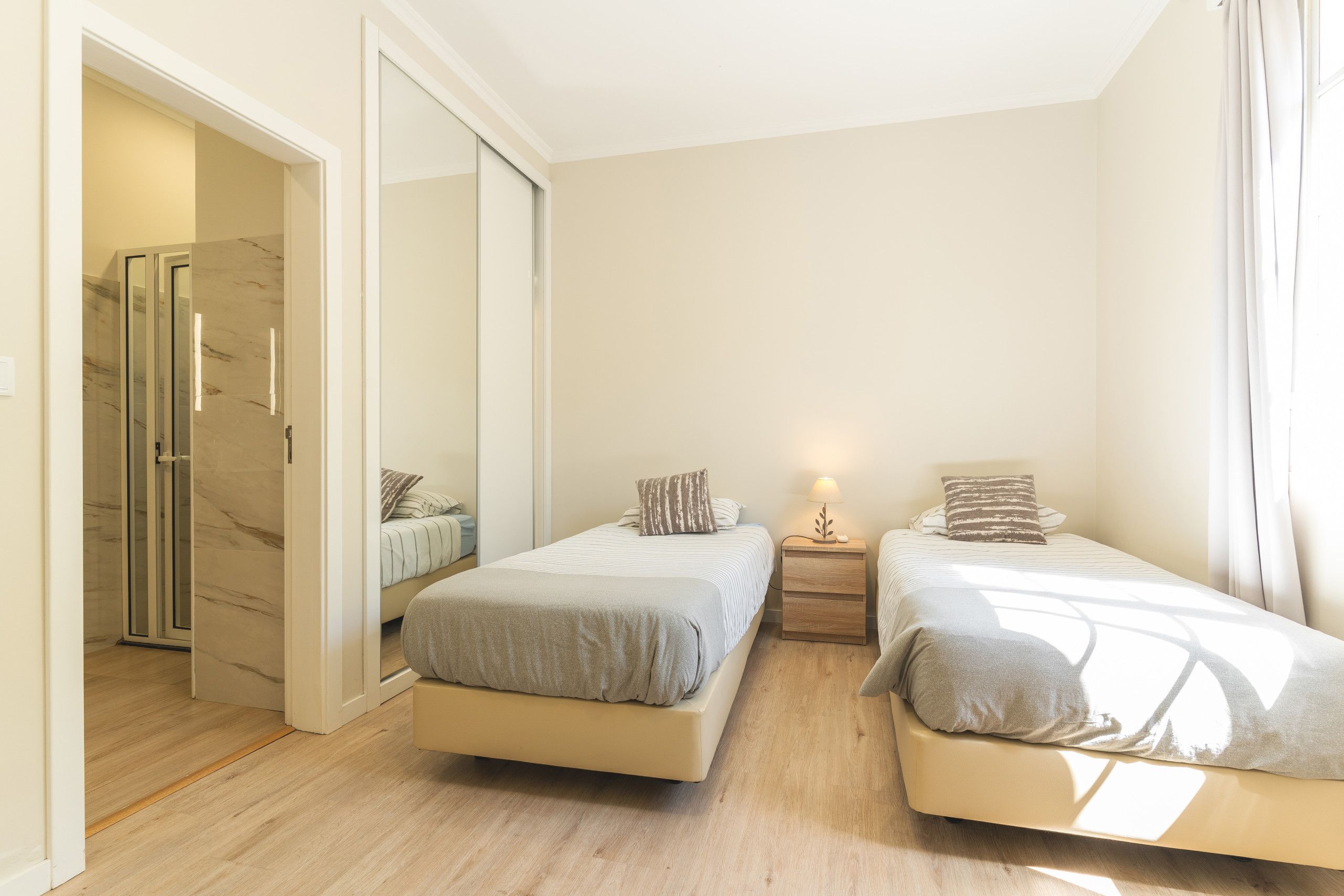A bedroom with two beds, a nightstand, a lamp, and a sliding door leading to a bathroom.