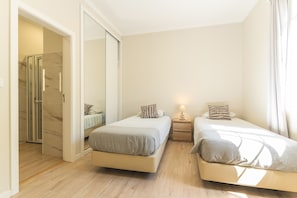 Un dormitorio con dos camas, una mesita de noche, una lámpara y una puerta corrediza que da a un baño.