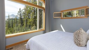 Un dormitorio con un gran ventanal que ofrece vistas a un bosque y montañas.