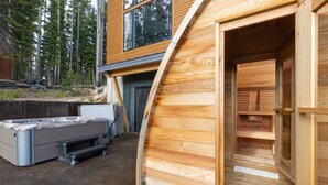 Una sauna de madera con una gran abertura, un jacuzzi y una pared de piedra al fondo.