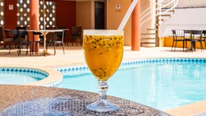A glass of tropical drink with a straw on a table by a poolside. - Pousada Mares Sergipe (Estancia)