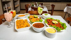 A dining table with various dishes, drinks, and a kitchen in the background. - Pousada Mares Sergipe (Estancia)