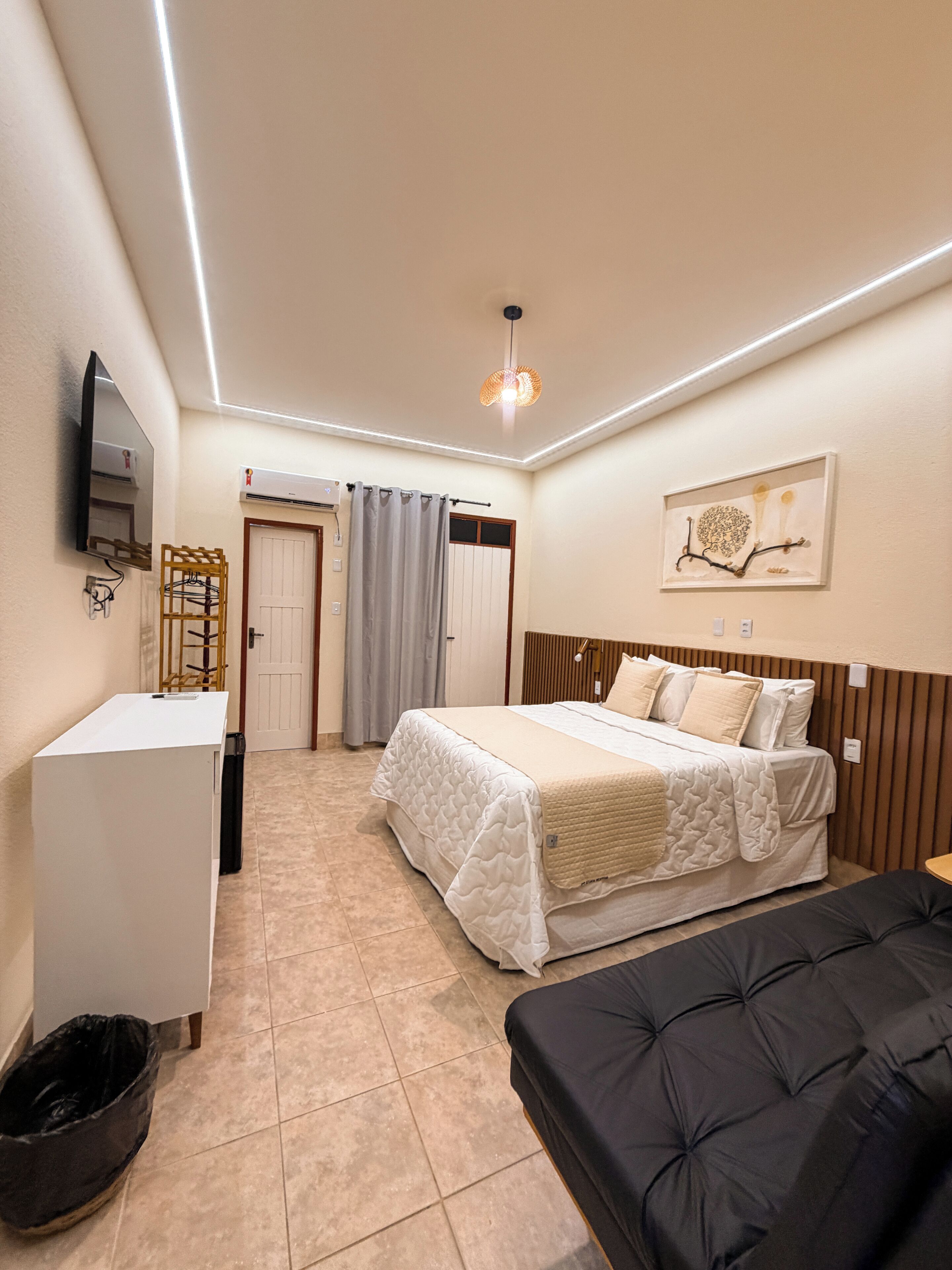 Habitació d'hotel amb un llit, una taula de treball, un televisor, un safataire i un quadre a la paret.