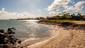 A beach with clear water, a sandy shore, and a distant shoreline with buildings and trees. - Pousada Mares Sergipe (Estancia)