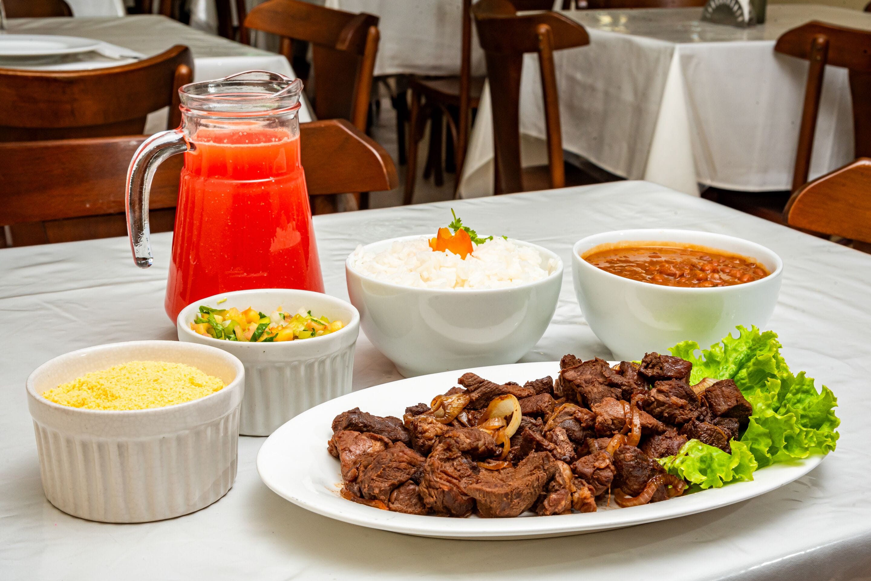 A dining table with a plate of meat, bowls of rice, and a pitcher of red drink.