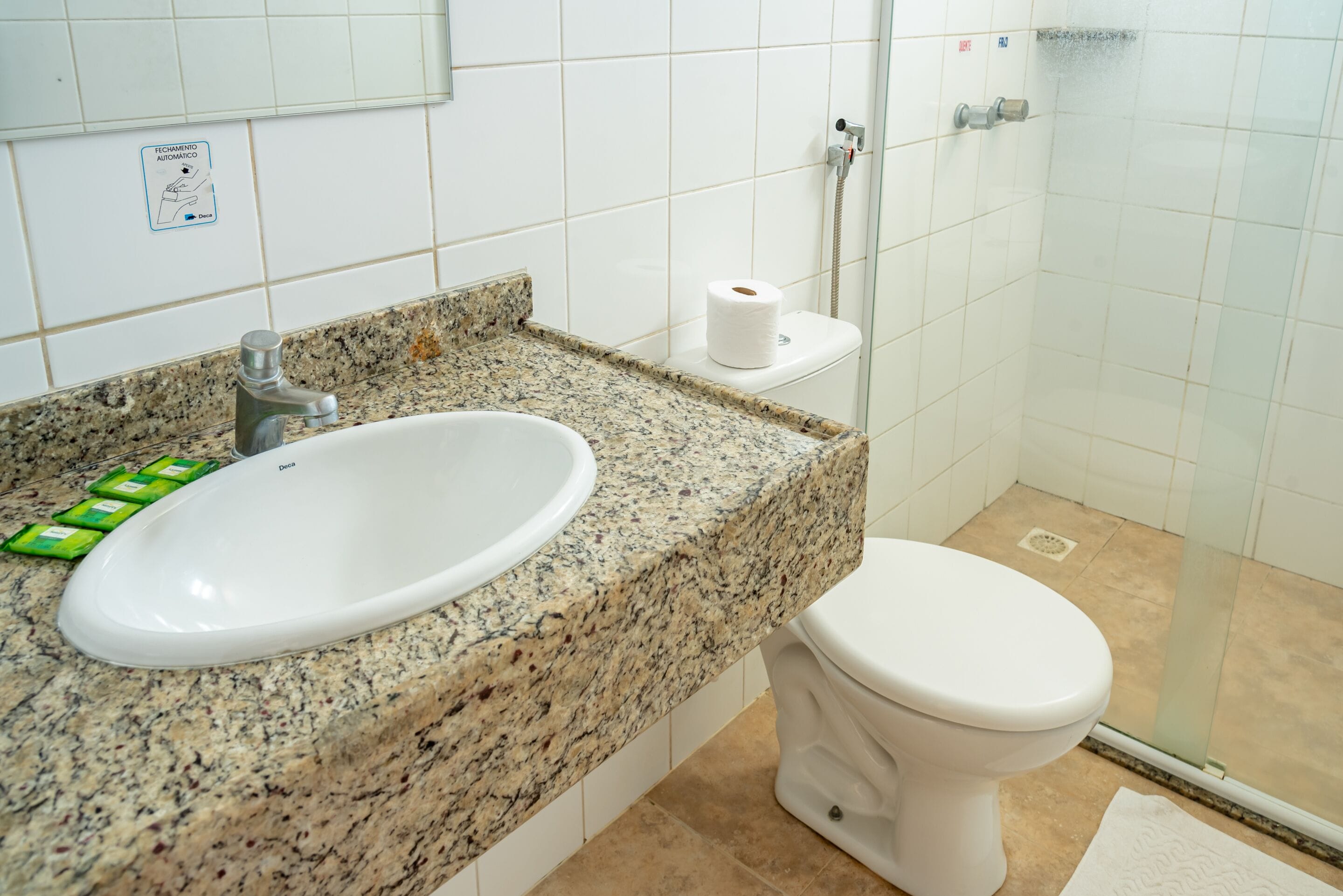 A bathroom with a granite countertop, a white sink, a toilet, and a glass shower enclosure.