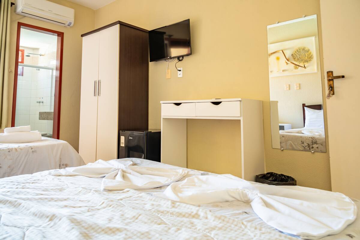 A hotel room with a bed, a wardrobe, a desk, a television, and a mirror.