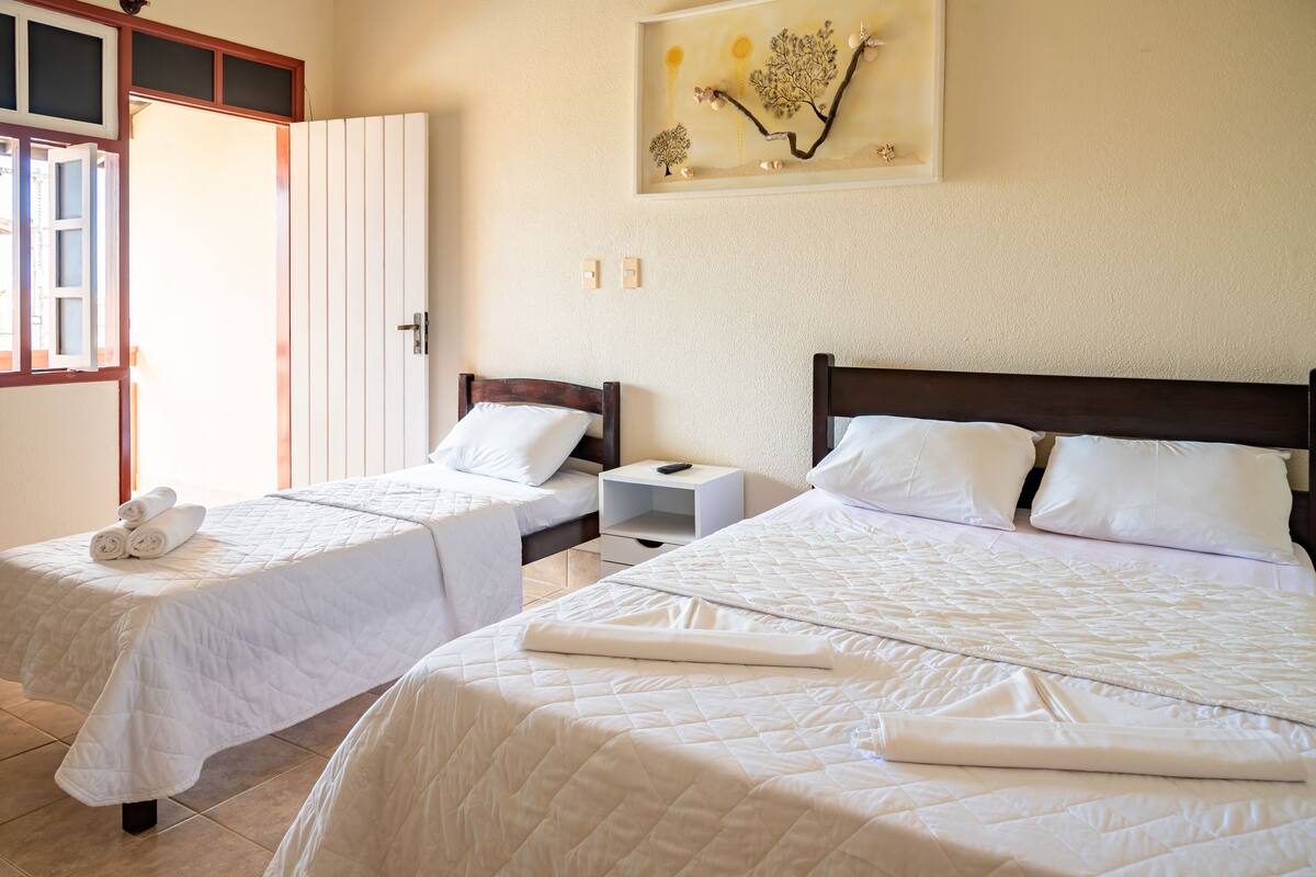 A hotel room with two single beds, a nightstand, a wall-mounted artwork, and a door leading to another room.