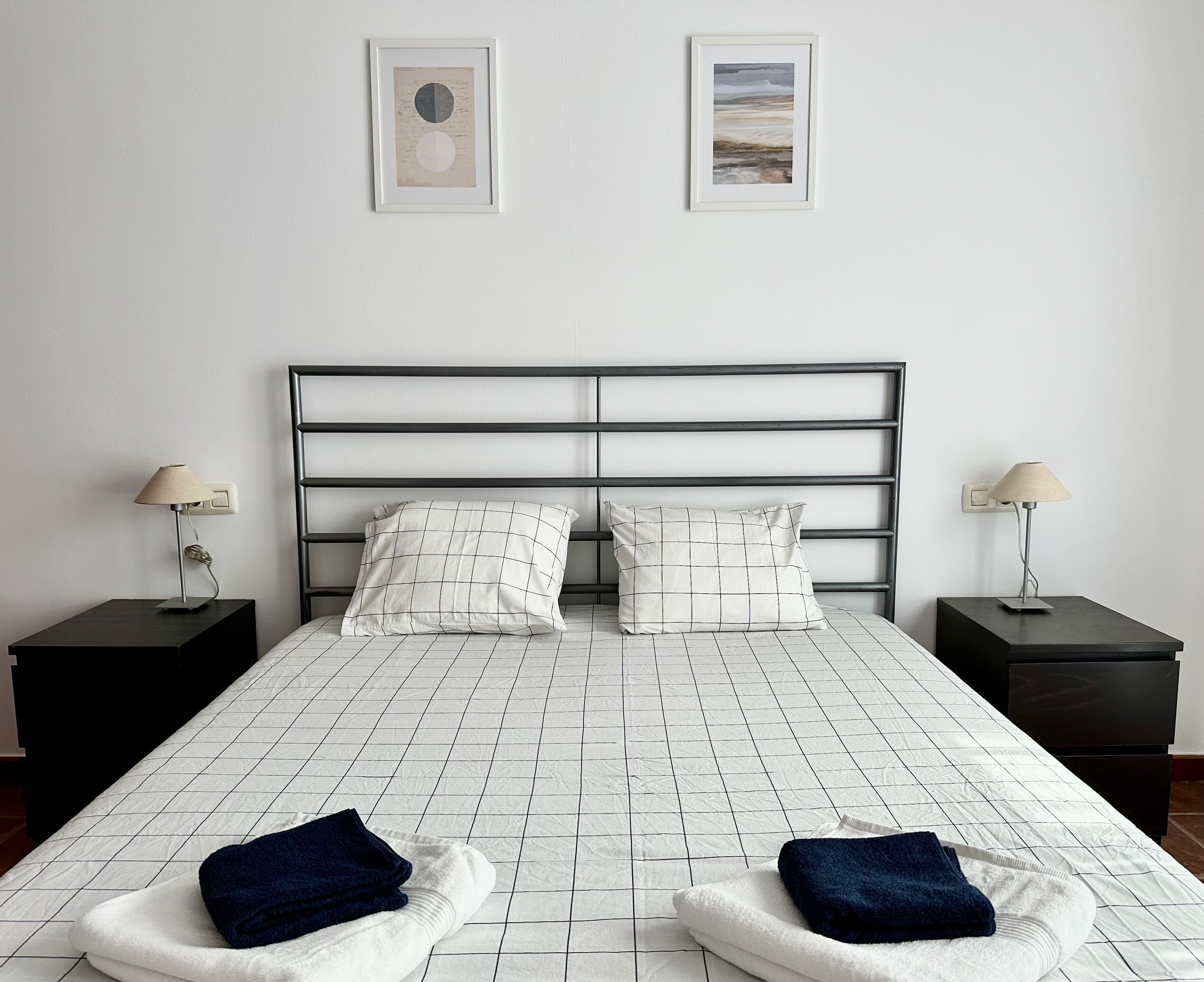 Un dormitorio con una cama, dos mesitas de noche, dos lámparas y dos cuadros en la pared.