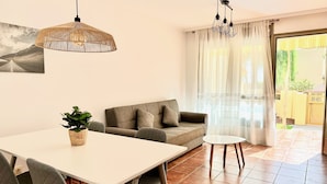 Ein modernes Wohnzimmer mit einer Couch, einem Esstisch mit Stühlen, einer Hängeleuchte und Blick ins Freie durch ein Fenster.