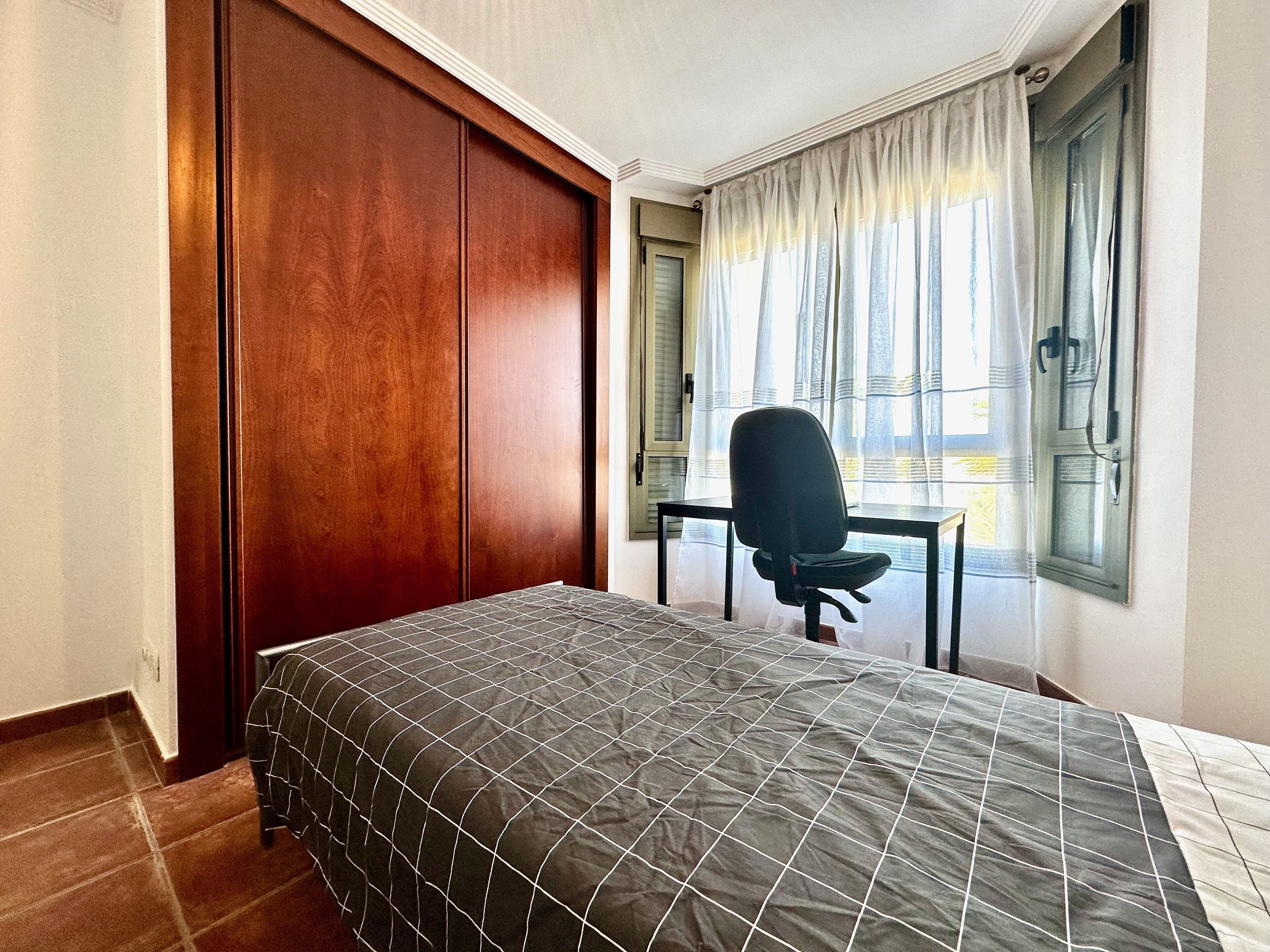 A bedroom with a bed, a desk, and a chair.