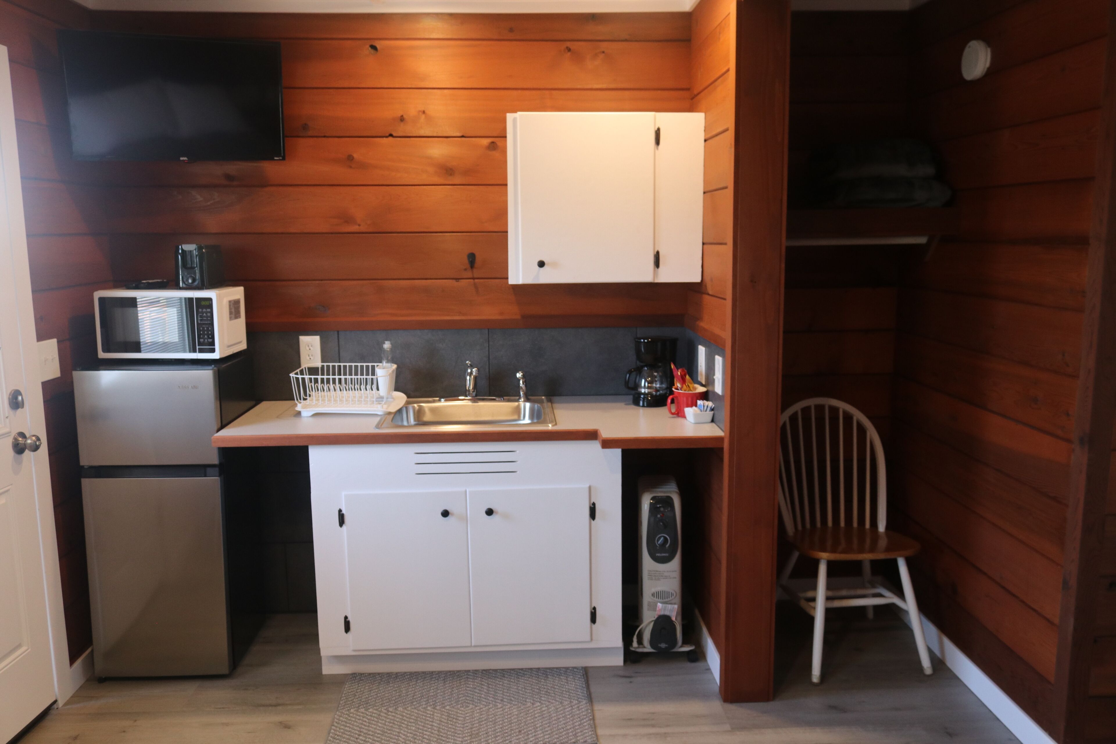 A compact kitchen with a microwave, refrigerator, sink, and a small cabinet.