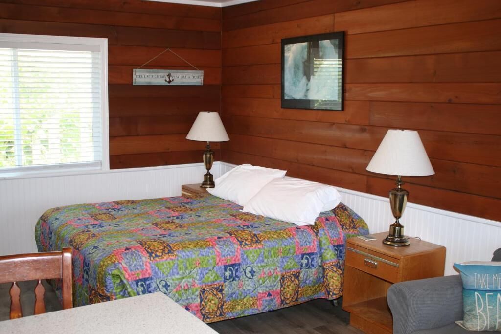 Una habitación acogedora con una cama, dos lámparas de noche, un cabecero de madera, una ventana con persianas y un reloj de pared.