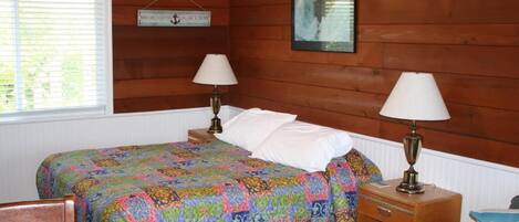 Una habitación acogedora con una cama, dos lámparas de noche, un cabecero de madera, una ventana con persianas y un reloj de pared.