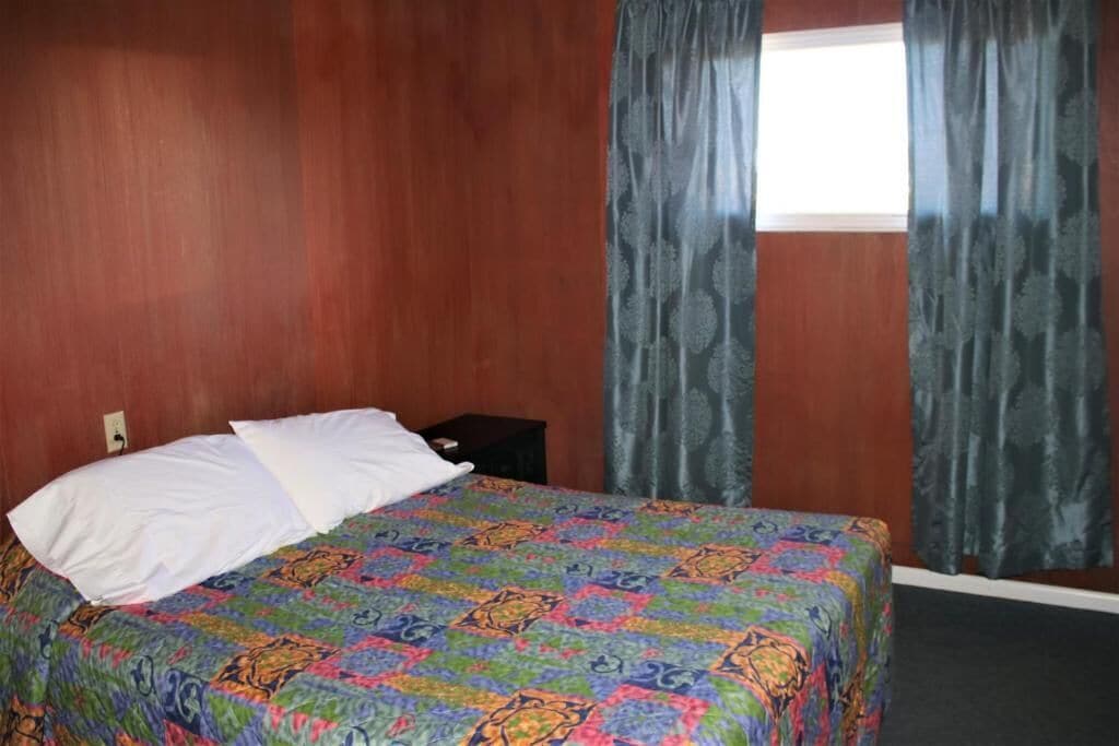 A hotel room with a bed, a nightstand, and a window with curtains.