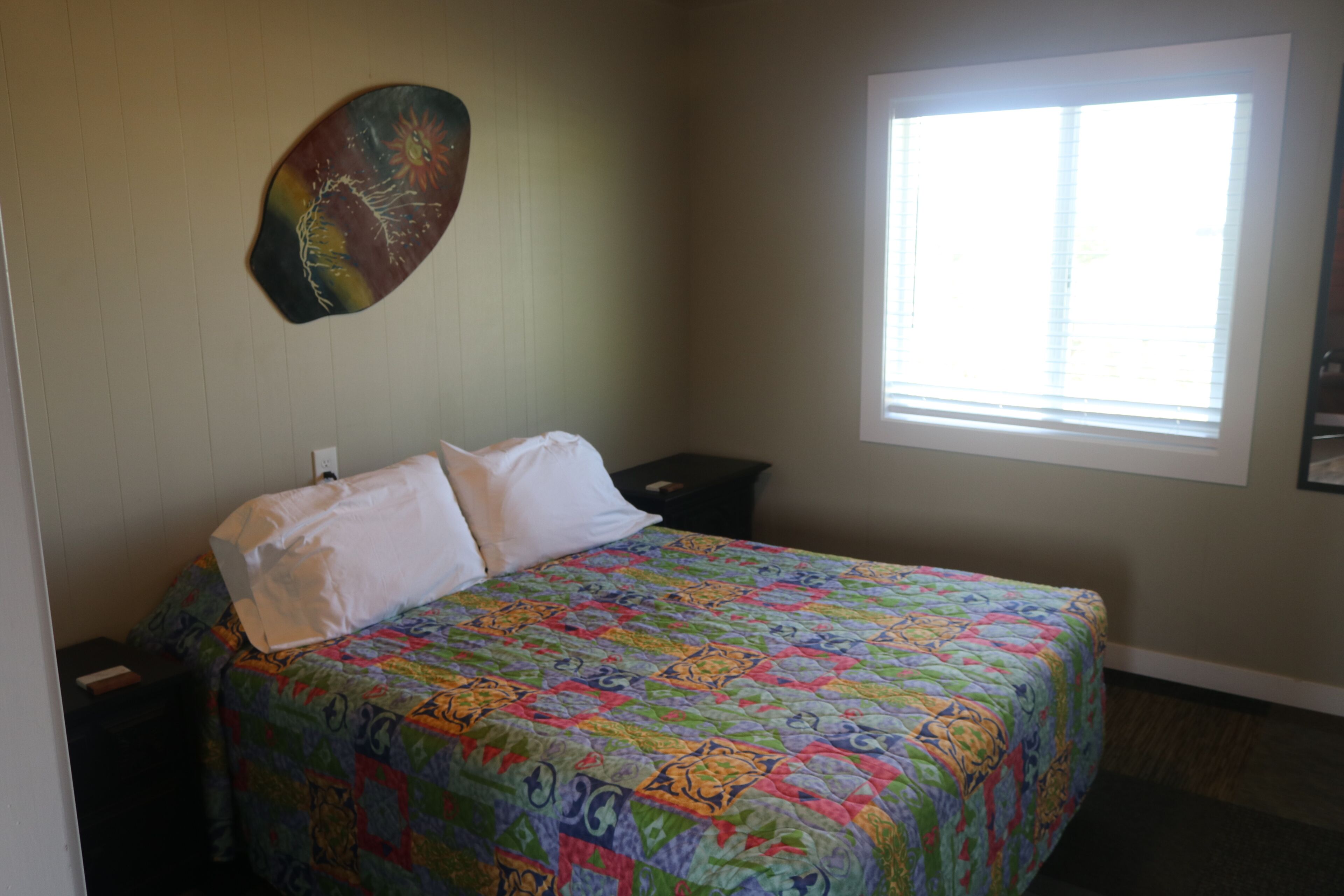 A bedroom with a bed, a nightstand, a window, and a wall decoration.