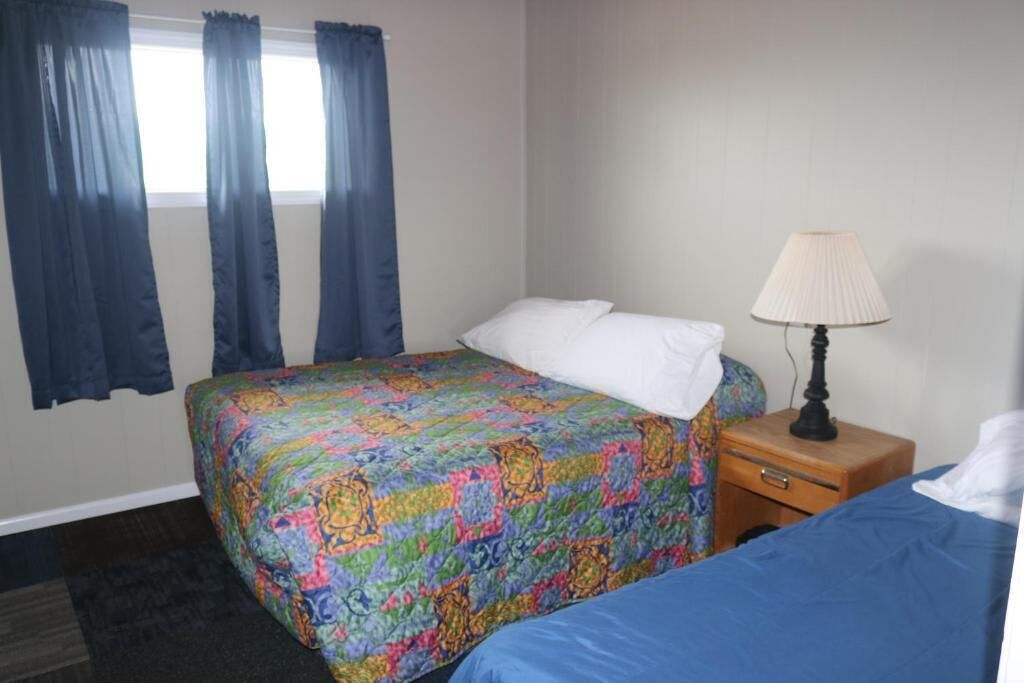 Een hotelkamer met een bed, een nachtkastje met een lamp en een raam met gordijnen.