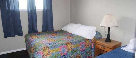 Een hotelkamer met een bed, een nachtkastje met een lamp en een raam met gordijnen.