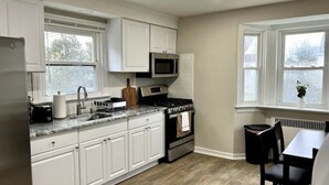 A kitchen with white cabinets, a microwave, an oven, a sink, and a dining area with a table and chairs.