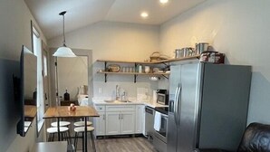 A compact kitchen with a dining area, a refrigerator, and a leather couch.